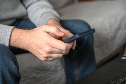 Čovjek sa modernim mobilnim telefonom u ruci. Muškarac drži pametni telefon u rukama. Mladić dodiruje ekran mobitela u svojoj kancelariji. Čovjek  koristi pametni telefon kod kuće.