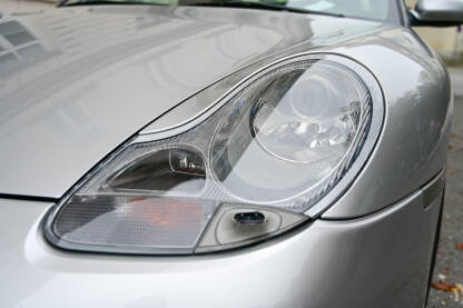 Far automobila, krupni plan. Prednja svjetla sivog automobila na parkingu u gradu. Farovi automobila Porsche.