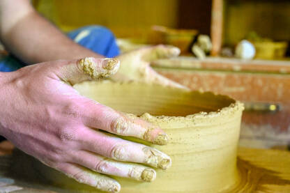 Profesionalni keramičar radi sa glinom. Obrtnik oblikuje glinu na lončarskom kolu u radionici. Ručni rad. Krupni plan lončara koji oblikuje glinu i pravi lonac.