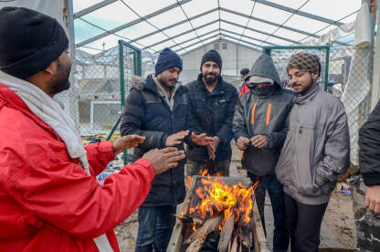 Grupa migranata se grije uz vatru u kampu. Migracije. Izbjeglice u Bosni i Hercegovini. Balkanska ruta.