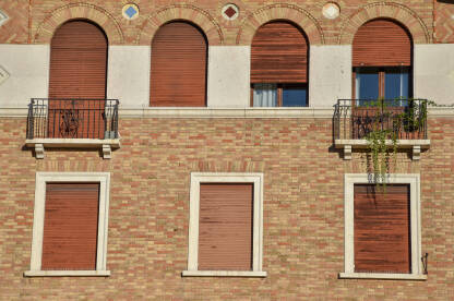 Prozori na zgradi napravljenoj od cigle. Zgrada u Padovi, Italija. Prozori sa spuštenim roletnama.