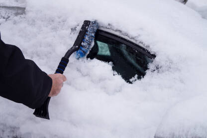 Vozač čisti auto od velikog snijega četkom.