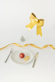 Božićni, novogodišnji stol s tanjurom, ukrasnom kuglicom, mašnom, vrpcom i šišarkom.