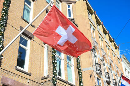 Nacionalna zastava Švicarske na zgradi. Bijeli križ na crvenoj pozadini. Švajcarska zastava.