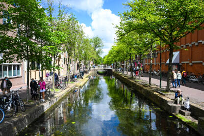Delft, Nizozemska: Zgrade i riječni kanal u gradu. Ljudi šetaju gradom.