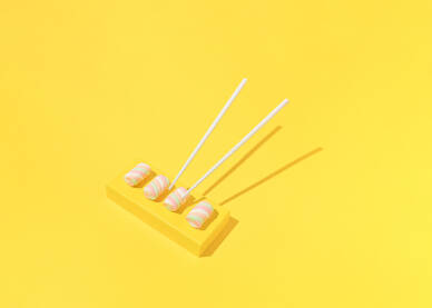 Spužvasti bomboni posluženi kao suši s kineskim štapićima za jelo na žutoj pozadini.