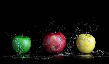 Tri vrste svježih jabuka uprskane vodom na crnoj pozadini