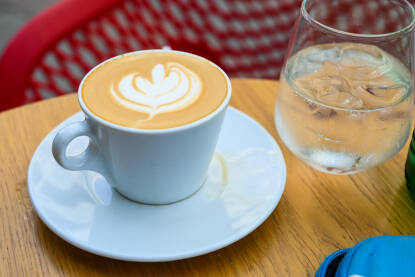 Kafa i mineralna voda na stolu u kafiću. Kafa sa mlijekom servirana u bašti kafića. Macchiato.