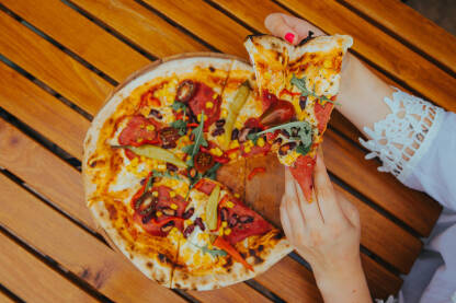 Pizza na drvenom stolu, djevojka uzima komad pizze