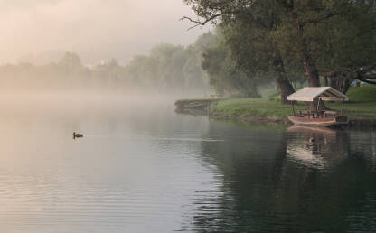 Mirno ljetno i maglovito jutro na rijeci sa drvenom lađom i patkom