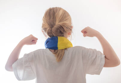Djevojčica snimljena s leđa, u bijeloj majici sa zastavom BiH oko vrata i stisnutim šakama kao signalom podrške. Navijač, podrška, BiH,  Bosna i Hercegovina.