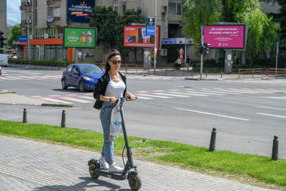 Žena vozi električni romobil u gradu. Prijevoz u gradu. Mlada žena vozi romobil.