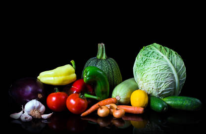 Svježe sezonsko povrće na crnoj pozadini. Glavica kupusa, tikva, paprike, patlidžan, krastavci, mrkva, luk, paradajz, limun i bijeli luk.