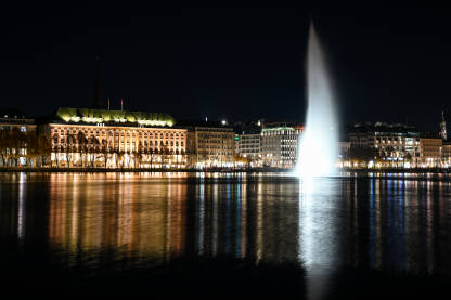 Hamburg, Njemačka. Toranj gradske vijećnice, zgrade i Alster jezera noću. Cityscape. Refleksija svjetla u vodi.
