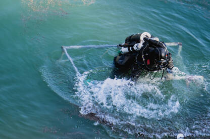 Ronilac izranja iz vode i ulazi u korpu za transport uz strmu obalu jezera. Ronioci, pod vodom, čiste naplavine materijala u jablaničkom jezeru.