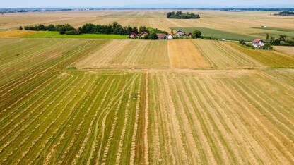 Polje nakon žetve ljeti i selo u daljini, snimak dronom.