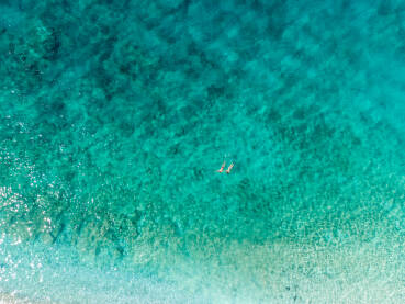 Turisti rone i plivaju u vodi. Snimak dronom na kupače u moru tokom ljeta. Prozirna morska voda u uvali.