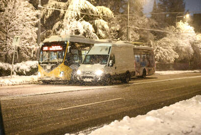 Trolejbus i vozila se kreću po snijegom pokrivenom putu. Javni gradski prevoz u Sarajevu. Vožnja vozila zimi dok pada snijeg. Pahulje snijega padaju na put. Zimska vožnja u gradu.
