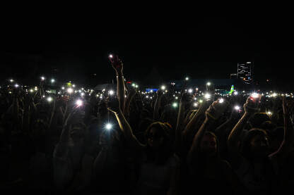 Ljudi drže mobilne telefone i upaljače na koncertu. Obožavatelji koriste svjetla pametnog telefona na muzičkom festivalu. Ljudi na koncertu su upali mobilne telefone na rock koncertu.