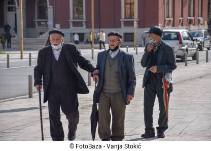 Stariji muškarci hodaju ulicom sa maskama na bradi. Trojica starijih muškaraca hodaju ulicom tokom pandemije virusa korona u Draču, Albanija.