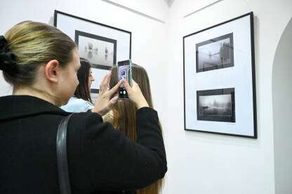 Ljudi na izložbi. Posjetioci posmatraju i fotografišu fotografije u galeriji.