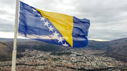 Državna zastava Bosne i Hercegovine se vijori na vjetru. Nacionalna zastava Bosne i Hercegovine na jarbol iznad grada Mostara, snimak dronom.
