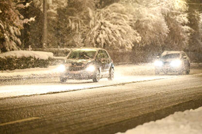 Automobili se kreću po snijegom pokrivenoj cesti. Vožnja vozila zimi dok pada snijeg. Pahuljice snijega padaju na cestu. Otežani i opasni uslovi vožnje.