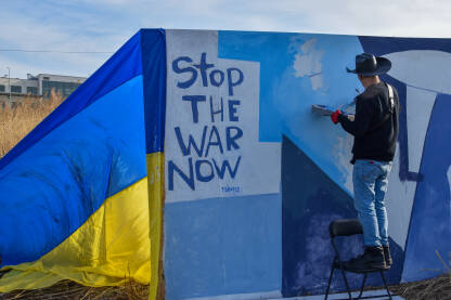 Muškarac crta mural na zidu, granica Poljska-Ukrajina, prelaz Medyka. Antiratni mural. Mirovna umjetnost. Doček izbjeglica iz Ukrajine. Zastava Ukrajine.