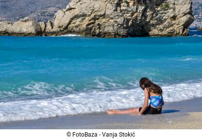 Lijep, sunčan dan na plaži u Ksamilu, Albanija. Djevojka sjedi sama na plaži. Tužna djevojka sjedi na obali mora.