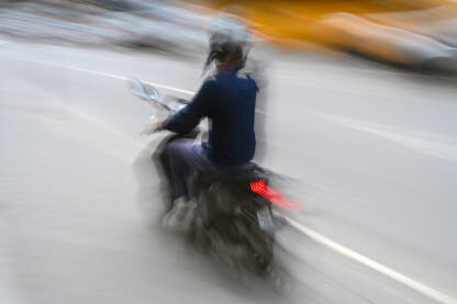 Čovjek se brzo kreće na motociklu ulicom. Čovjek se brzo kreće na motociklu ulicom. Vožnja skutera u gradu. Vozač motocikla.
