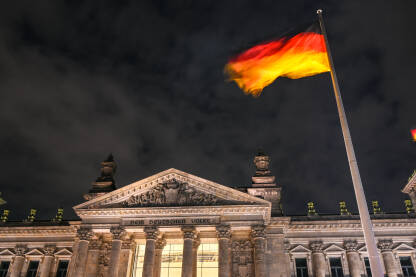 Njemačka državna zastava se vijori na jarbolu ispred zgrade Reichstaga u Berlinu, Njemačka. Državni i nacionalni simbol. Njemački Bundestag.