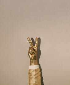 Ruka obojena u zlatnu boju s podignuta dva prsta kao znak mira.