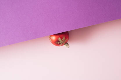 Crvena ukrasna kuglica na ružičastoj pozadini. Božićna, Novogodišnja čestitka.