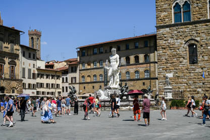 Firenze, Italija: Turisti istražuju grad. Neptunova fontana na Piazza della Signoria. Ljudi šetaju trgom. Zgrade u centru grada.