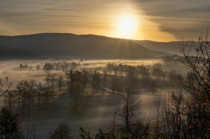 Izlazak sunca iznad sela. Magla je prekrila dolinu i drveće. Jesenje jutro.