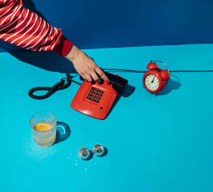 Minimalan retro koncept s rkoja podiže slušalicu crvenog telefona, te sat / časovnik, čaša alkohola i disko kugle na plavoj pozadini.