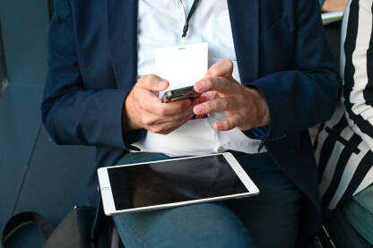 Čovjek koristi mobilni telefon i tablet na sastanku. Muškarac u odijelu drži pametni telefon u rukama.