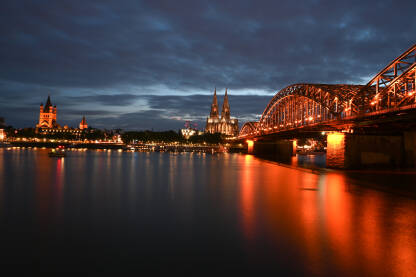 Köln, Njemačka. Poznati most Hohenzollern. Zgrade u staroj gradskoj jezgri. Tornjevi katedrale i gradske vijećnice noću.