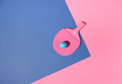 Roze reket za stolni tenis s plavom lopticom na plavoj i roze pozadini.
