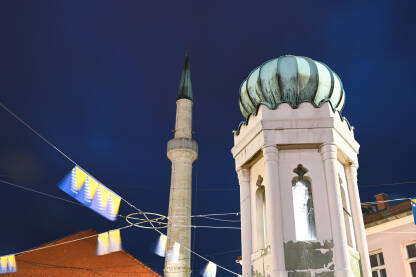 Česma i džamija na trgu u centru Tuzle sa zastavama Bosne i Hercegovine. Centralni trg u Tuzli.