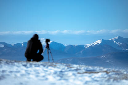 Fotograf sa opremom na vrhu brda snima planine pod snijegom