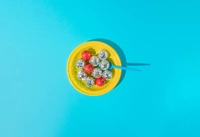 Žuti plastični tanjur s cherry rajčicama, disko kuglama i plavom plastičnom kašikom.