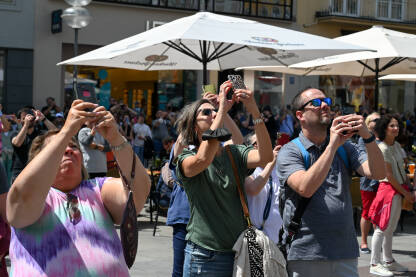 Ljudi fotografišu i snimaju mobilnim telefonima u centru grada. Turisti sa mobilnim telefonima u rukama.