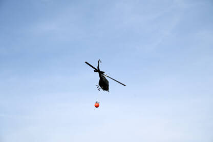 Helikopter u akciji gašenja požara u šumi. Helikopter leti sa kantom za vodu.