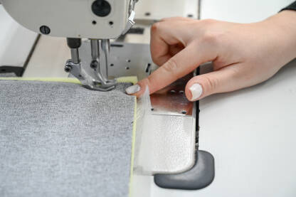 Žena šije tekstil šivaćom mašinom. Radnica radi u fabrici.
​