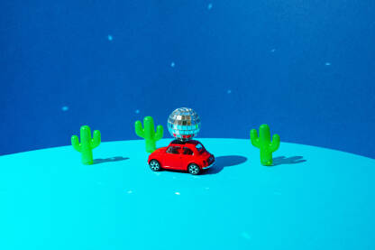 Disko kugla na krovu crvenog automobila i plastični kaktusi na plavoj pozadini.