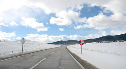 Snježni put zimi. Saobraćajni znak uz asfaltni put u prirodi.