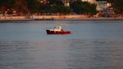 Manja crveno-bijela brodica usidrena na moru u predvečerje nedaleko od obale Podgore, grada u Hrvatskoj