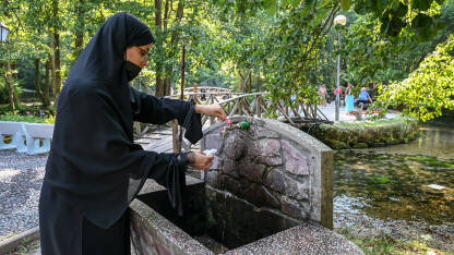 Žena sa nikabom sipa vodu u flašu iz česme. Vrelo Bosne, popularna turistička destinacija u BiH.