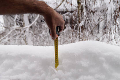 Čovjek mjeri dubinu snijega metrom.
